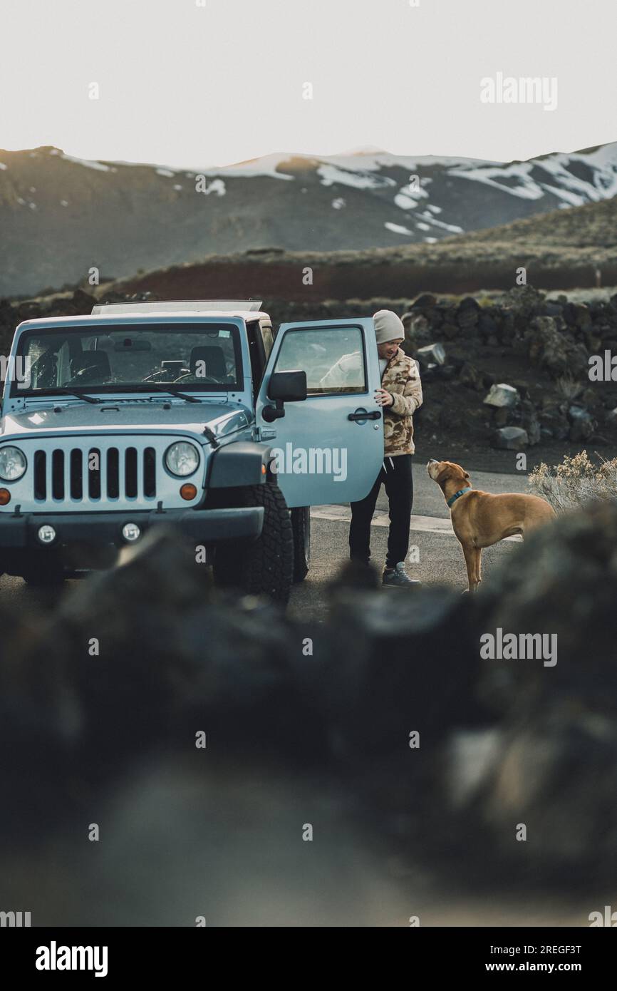 Der Hund starrt den Besitzer auf einem Roadtrip neben dem blauen Jeep an Stockfoto