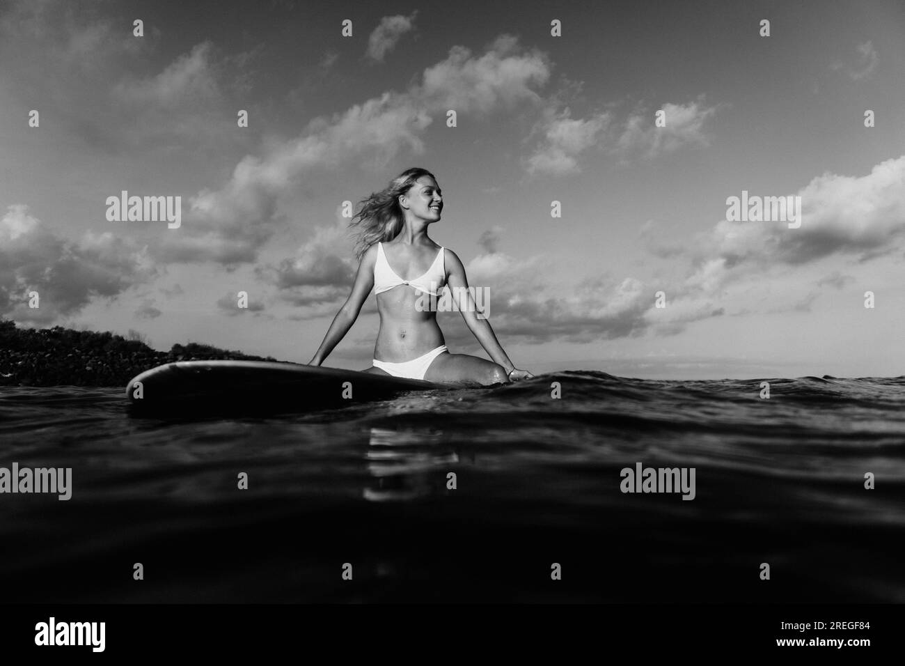 Eine junge Frau sitzt auf einem Surfbrett im Meer. Stockfoto