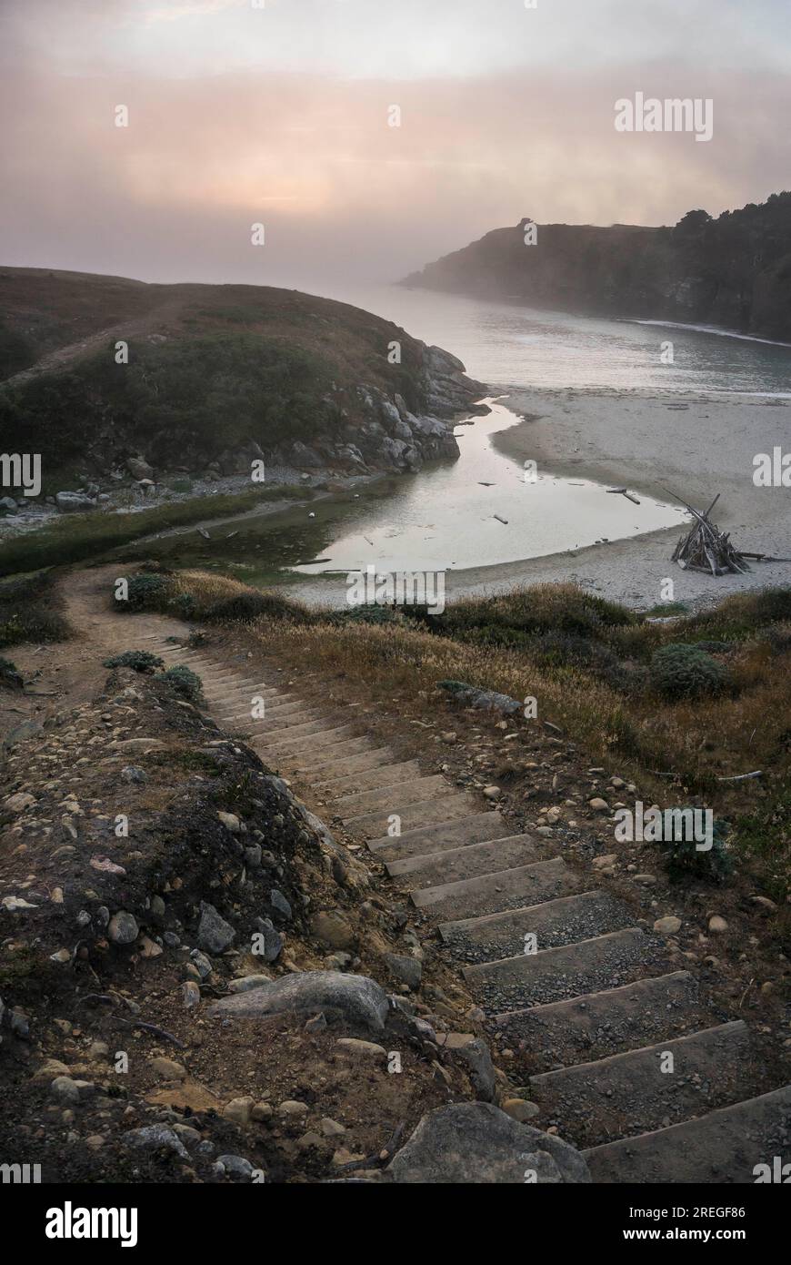 Treppen führen zu einem Strand mit Nebel und Sonnenuntergang Stockfoto