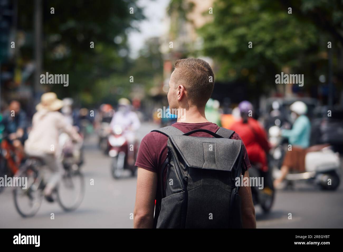 Reisende mit Rucksack, die Vietnam entdecken. Ein Mann mitten in einer belebten Straße voller Motorräder und Fahrräder in Hanoi, Vietnam. Stockfoto