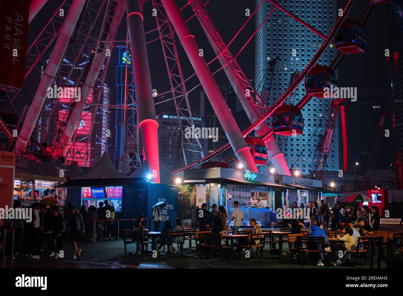 Hongkong, China - April 2. 2023: Menschenmenge unter dem Riesenrad am Hafen mit städtischen Nachtlichtern Stockfoto