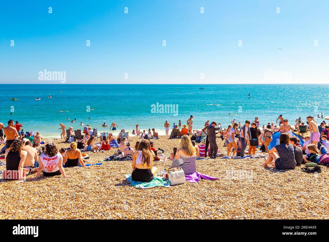 Leute, die an einem heißen Sommertag am Strand sitzen, mit Brighton Palace Pier im Hintergrund, Brighton, Großbritannien Stockfoto