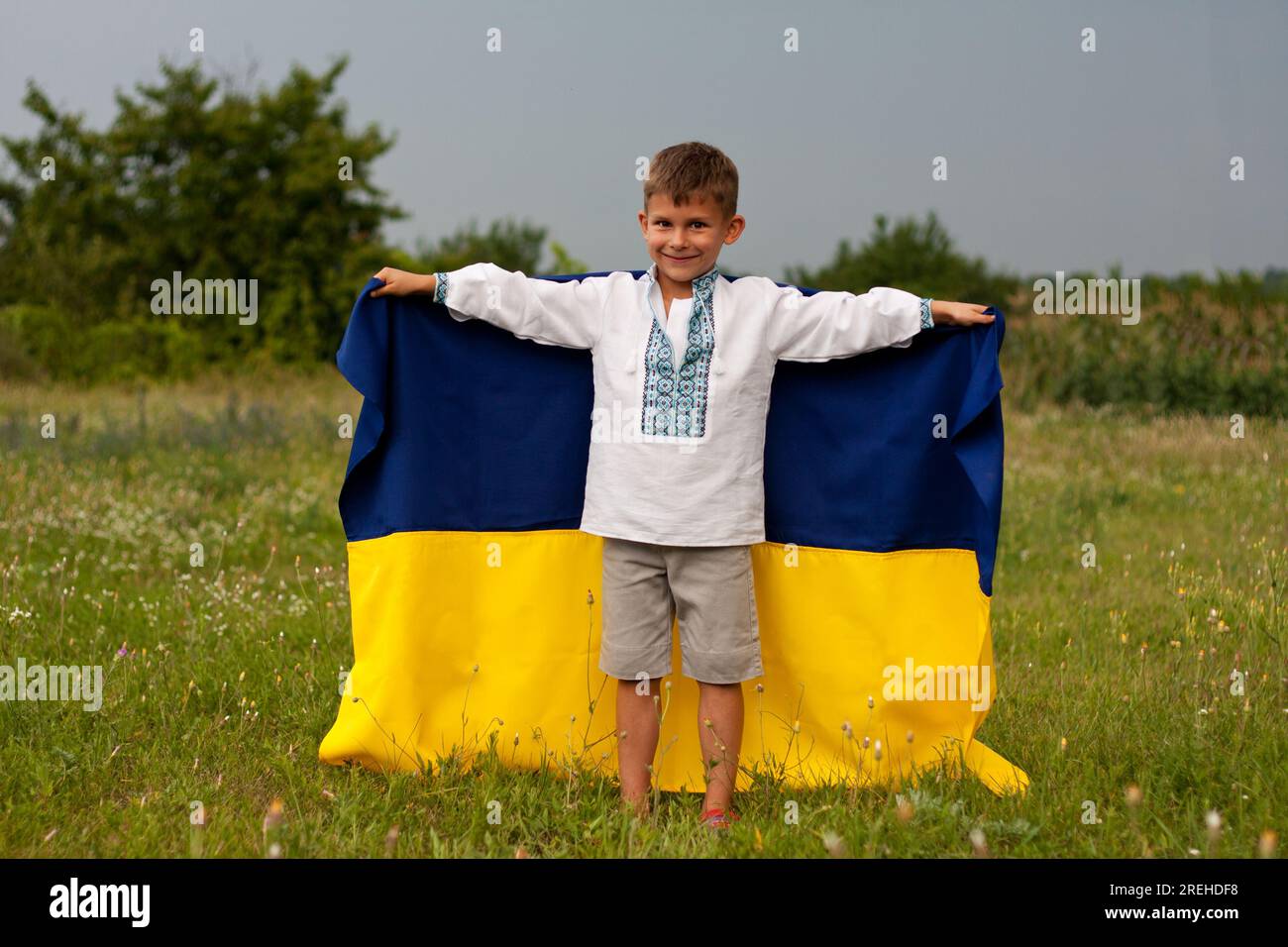 Ukrainischer Junge in besticktem Hemd-vyshyvanka, der am Sommertag auf Wiese die blau-gelbe Flagge der Ukraine demonstriert. Unabhängigkeitstag der Ukraine. Verstopfung Stockfoto