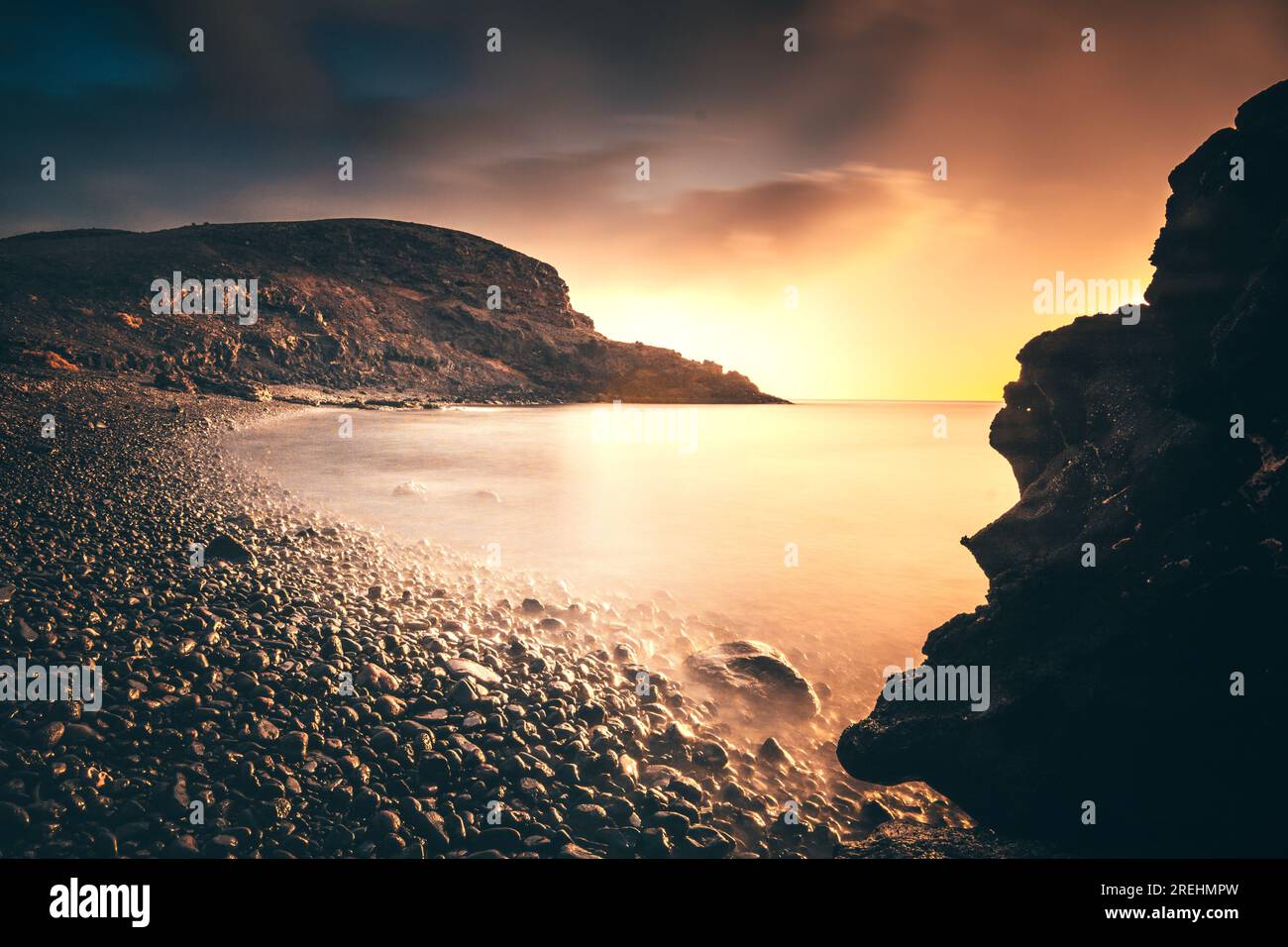 Sonnenaufgang oder Sonnenuntergang auf den Kanarischen Inseln von Fuerteventura. Am Strand mit Steinen und langer Exposition. Einzigartiges Licht. Urlaubskomfort pur. Schöne Wolken Stockfoto