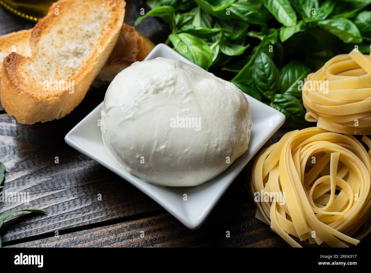 Italienische Zutaten, frischer Mozzarella, Bruschetta, rohe Tagliatelle und Basilikumblätter auf dunklem Holzhintergrund Stockfoto