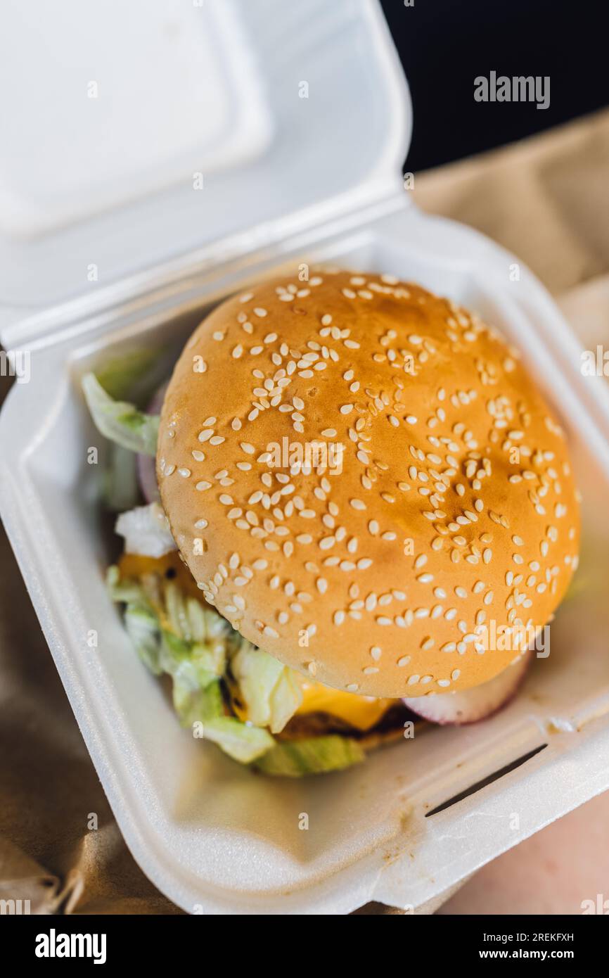 Klassischer Burger mit Sesambrötchen in einer Styroporbox ...