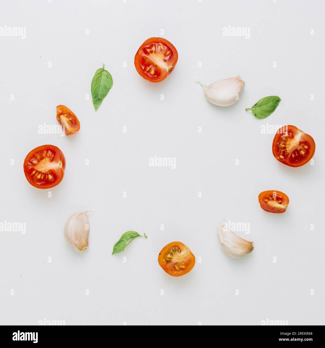 Runder Rahmen aus Kirschtomaten, Basilikum, Knoblauchzehen, weißer Hintergrund. Auflösung und hochwertige Fotos Stockfoto