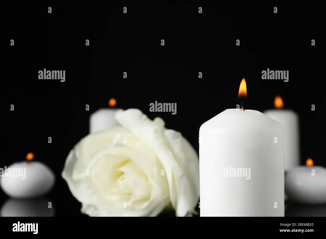 Weiße Rose und brennende Kerze im Dunkeln, Nahaufnahme mit Platz für Text. Begräbnissymbole Stockfoto