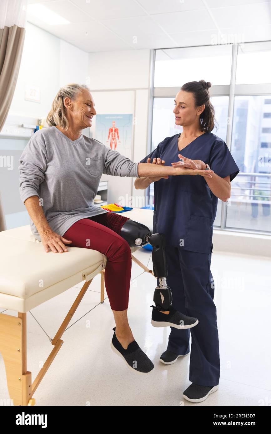 Kaukasische Physiotherapeutin und Seniorin mit künstlichem Beinmassearm im Krankenhaus Stockfoto