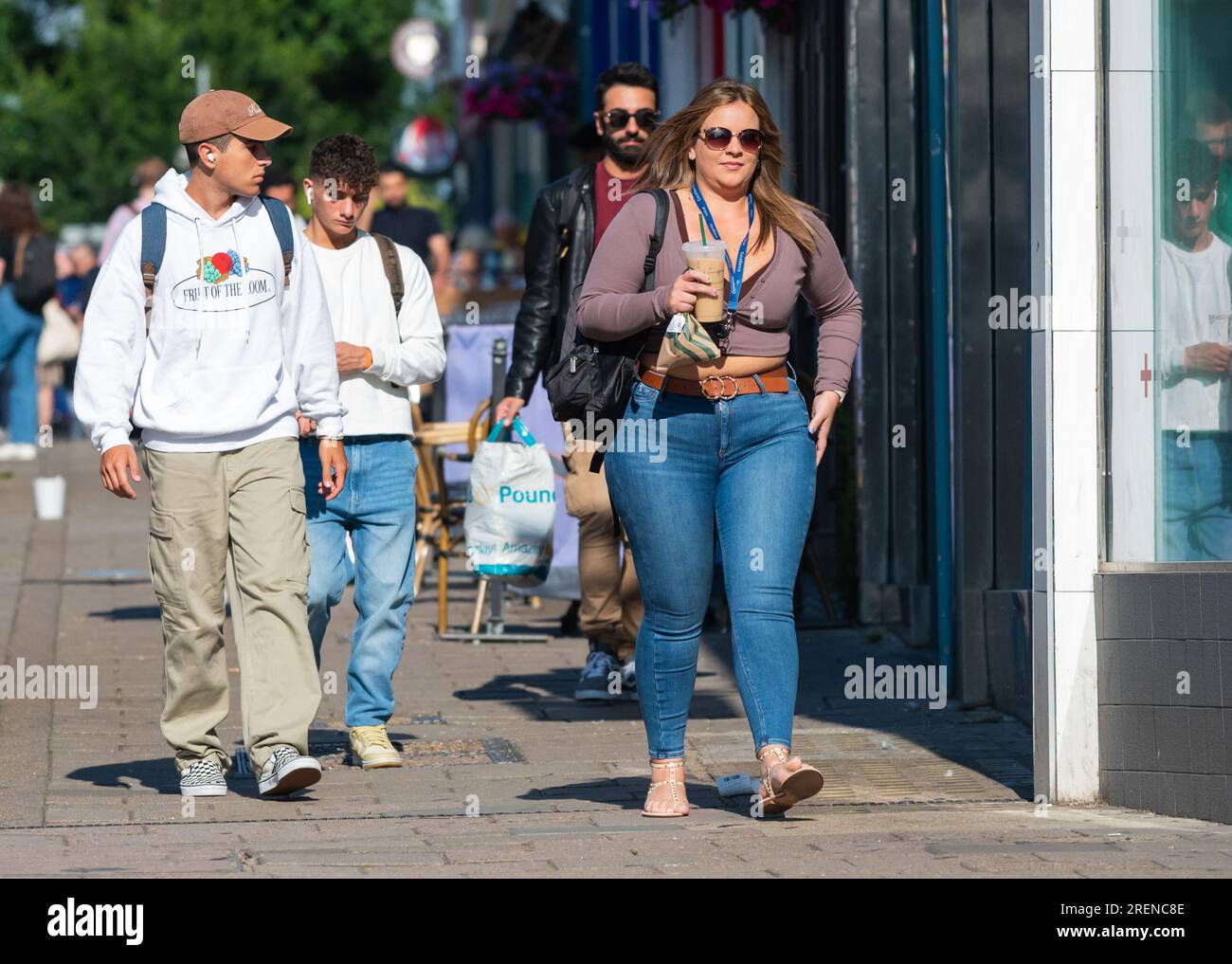 Hübsche junge Frau in Jeans, modisch gekleidet, in der geschäftigen Stadt unterwegs, mit einem Mitnahmegetränk, Schultertasche, im Sommer in Großbritannien. Fußgänger. Stockfoto