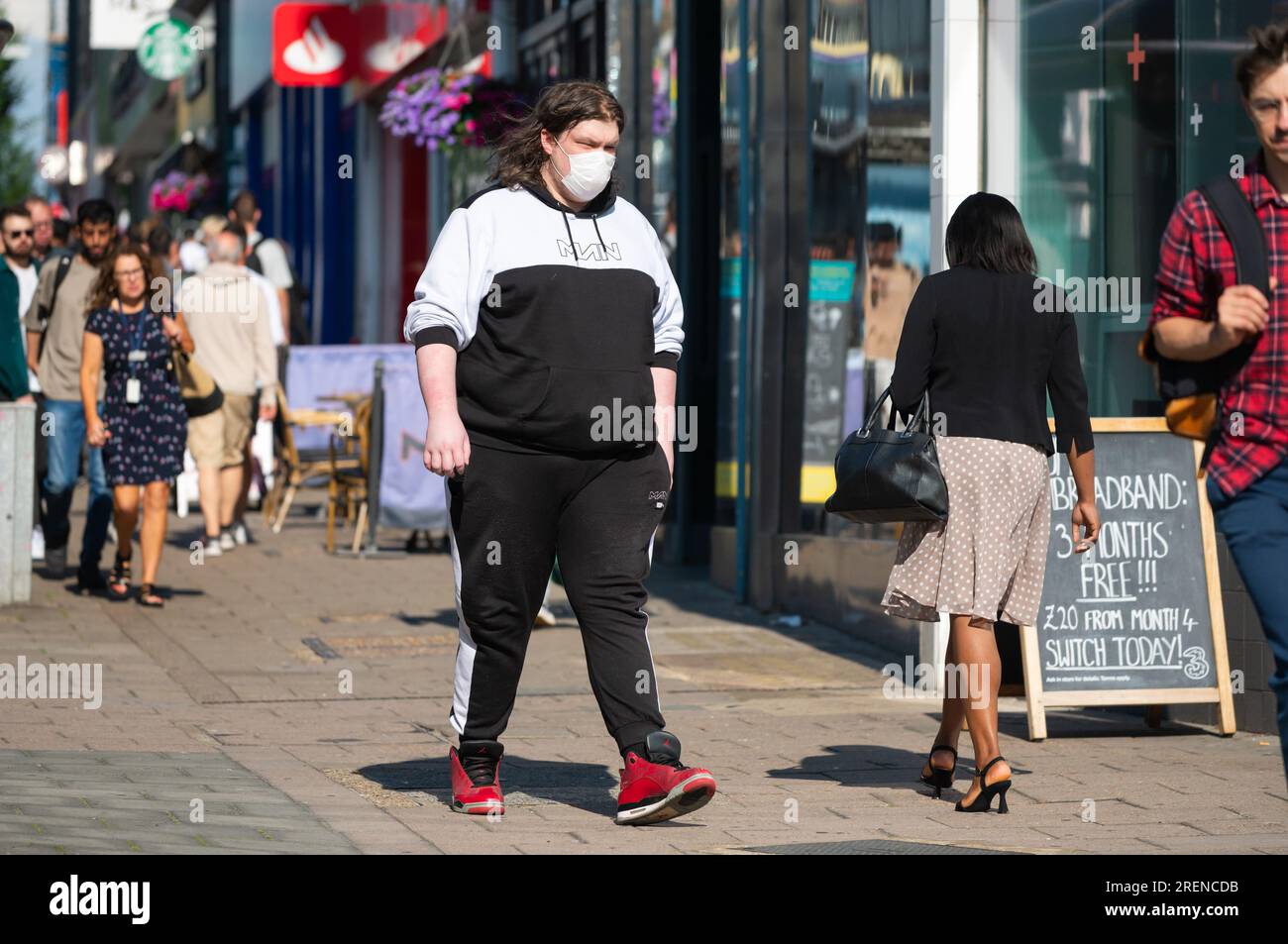 Übergewichtiger Mann, der in einer geschäftigen Einkaufsstraße in Summer, Großbritannien, mit Gesichtsmaske läuft. Stockfoto
