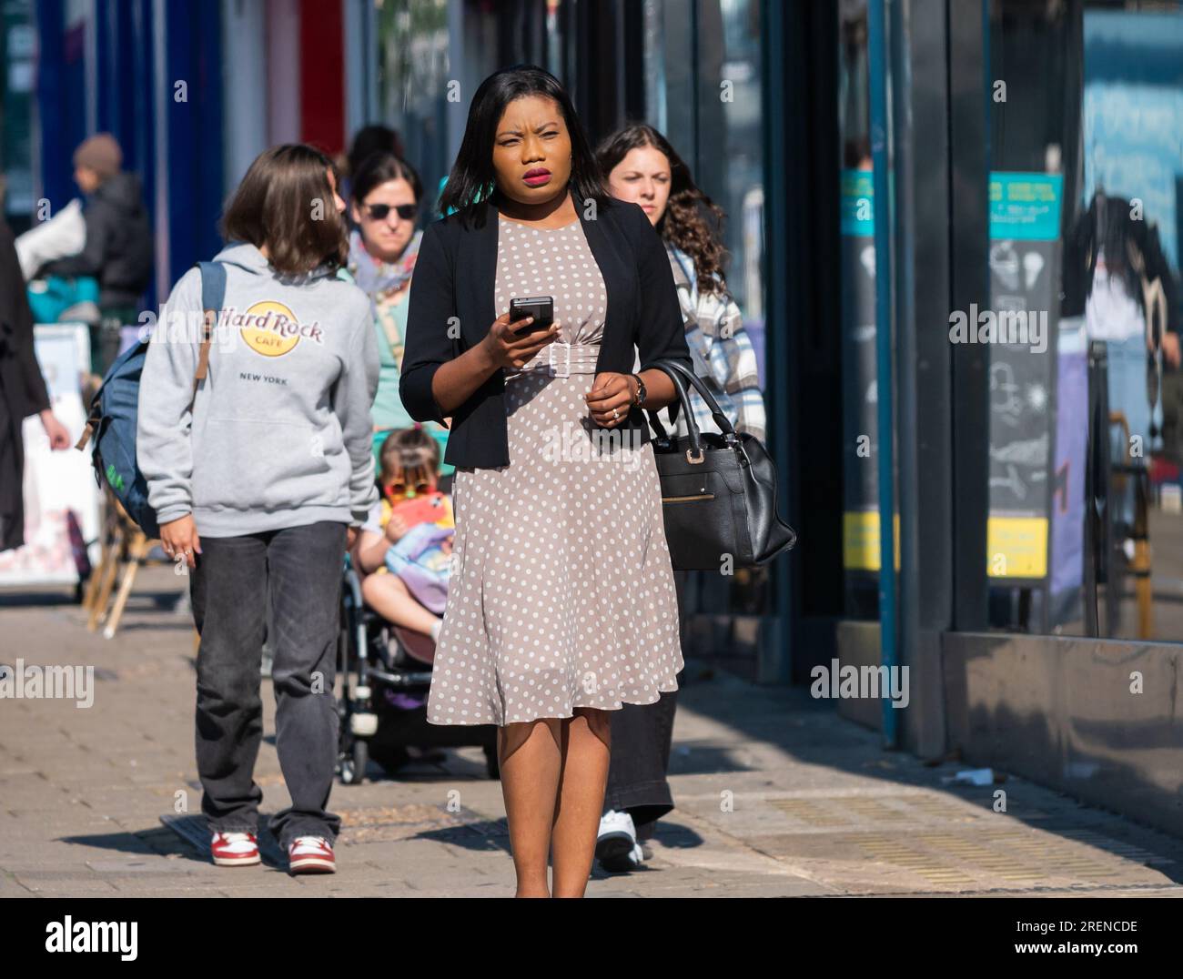 Hübsche junge Frau, modisch gekleidet, läuft in der geschäftigen Stadt mit Smartphone, im Sommer, Großbritannien. Stockfoto