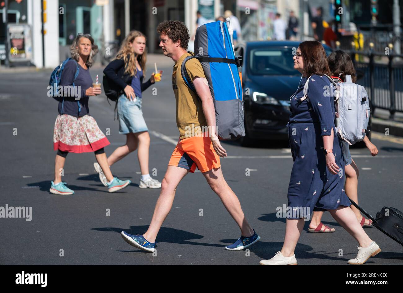 Menschen, die eine verkehrsreiche Straße in einer Stadt überqueren und einem Mann mit einem riesigen Rucksack oder Rucksack auf dem Rücken im Sommer in Großbritannien zeigen. Stockfoto