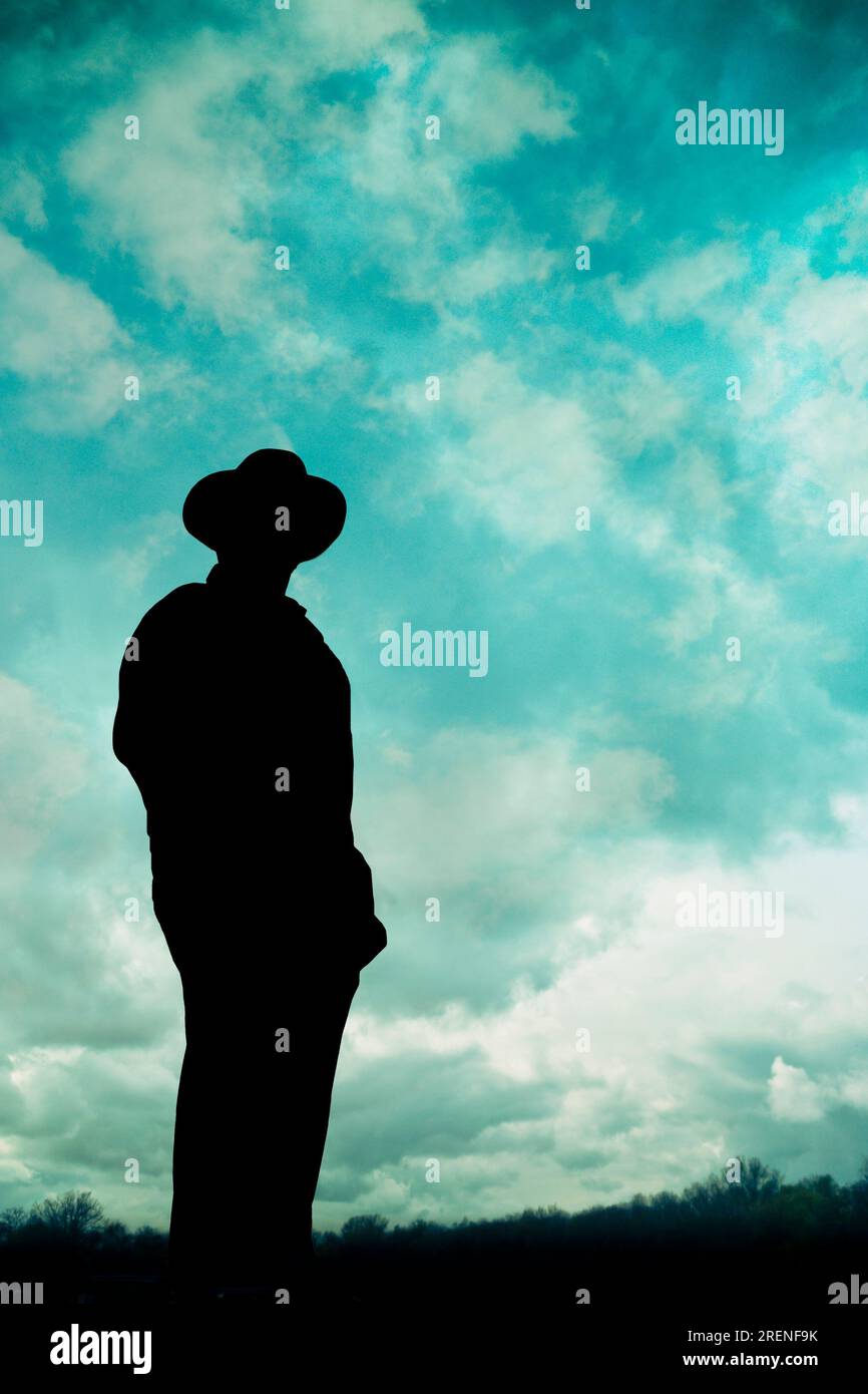 Silhouette eines Mannes mit Hut, der vor einem wolkigen Himmel steht Stockfoto