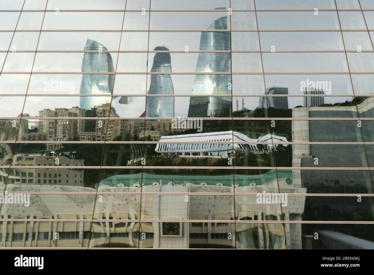 Baku, Aserbaidschan - 28. Juni 2023: An einem bewölkten Morgen werfen die berühmten Flammentürme ihre schimmernden Reflexionen auf die Fenster eines nahe gelegenen Einkaufszentrums Stockfoto