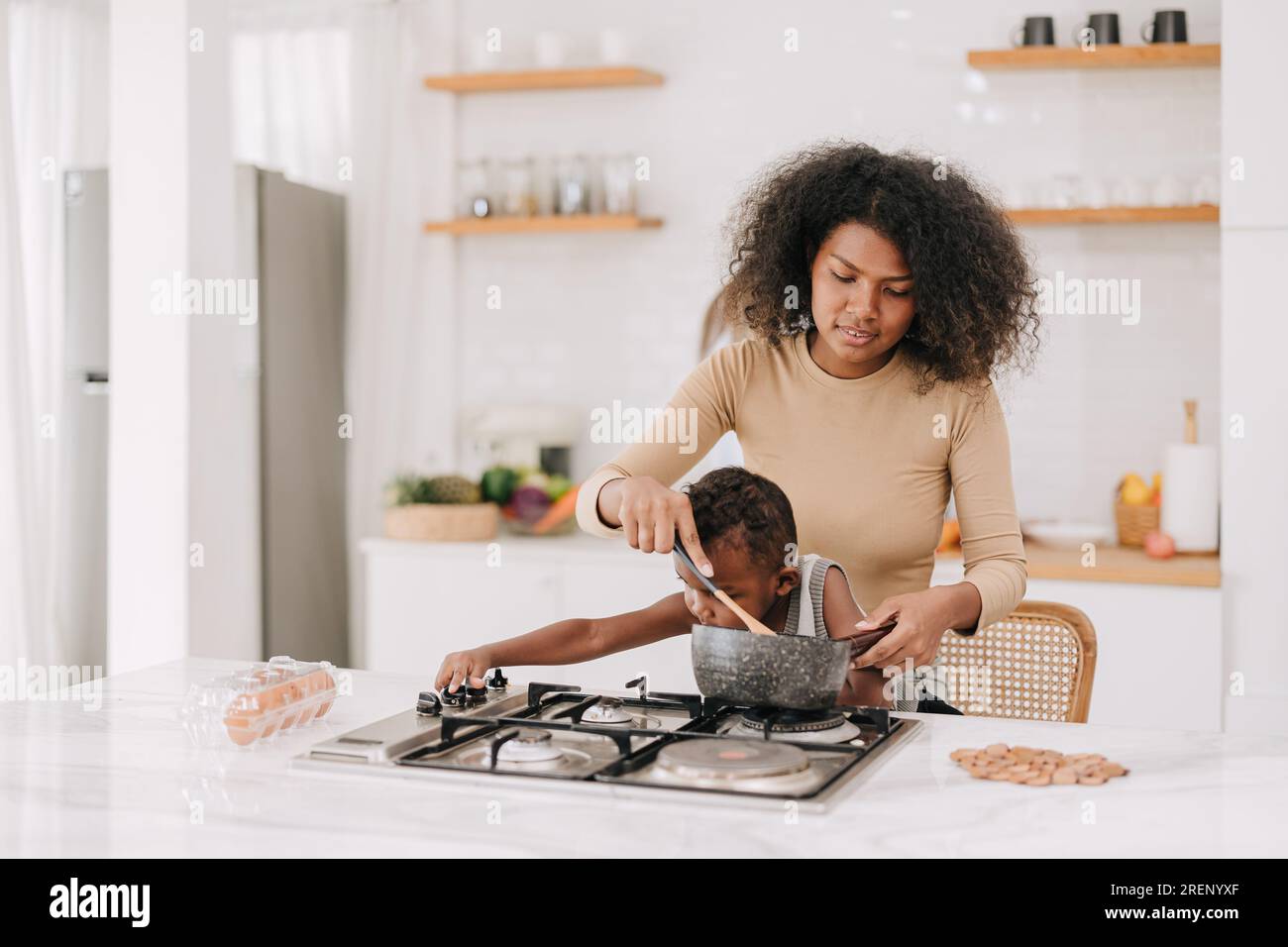 Beschäftigte mutter kocht zu Hause in der Küche auf der Herdinsel mit verspieltem, bösen Jungen Lebensstil im Vintage-Stil Stockfoto