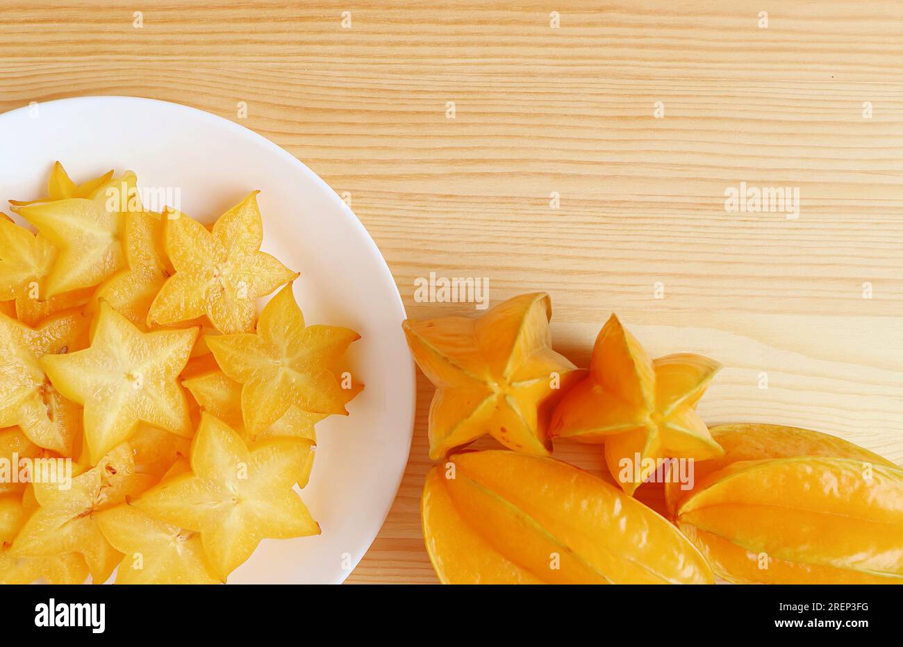 Ein Haufen frischer, reifer Sternenfrucht mit einem Teller leckerer, saftiger Scheiben auf einem Holztisch Stockfoto