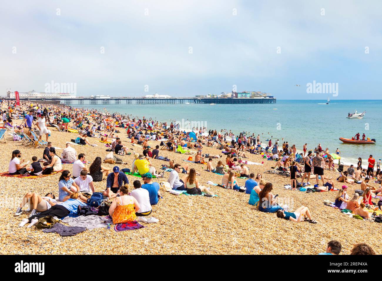 Leute, die an einem heißen Sommertag am Strand sitzen, mit Brighton Palace Pier im Hintergrund, Brighton, Großbritannien Stockfoto
