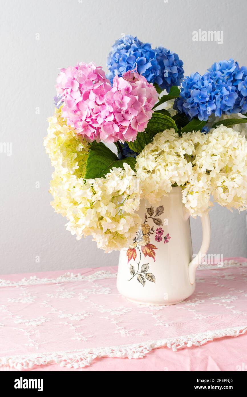 Wunderschöner Sommerstrauß mit rosa, lila und weißen Hortensien in einer Vase, gemütliche Inneneinrichtung, Tisch mit pinkfarbener Tischdecke und Blumenstrauß Stockfoto