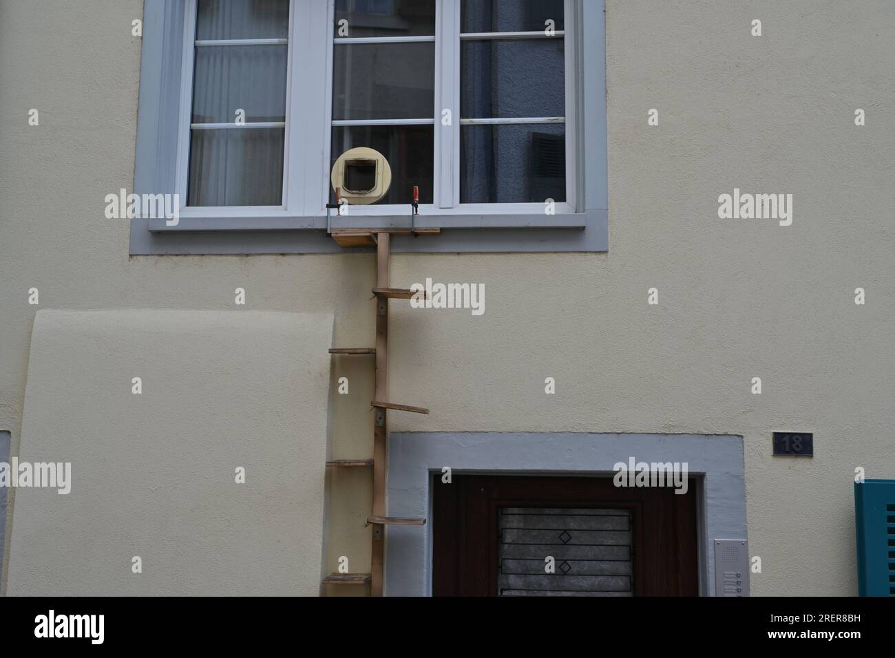 Ein Haus mit einem Fenster für eine Katze mit weißen Rahmen und einer hölzernen vertikalen Leiter. Stockfoto
