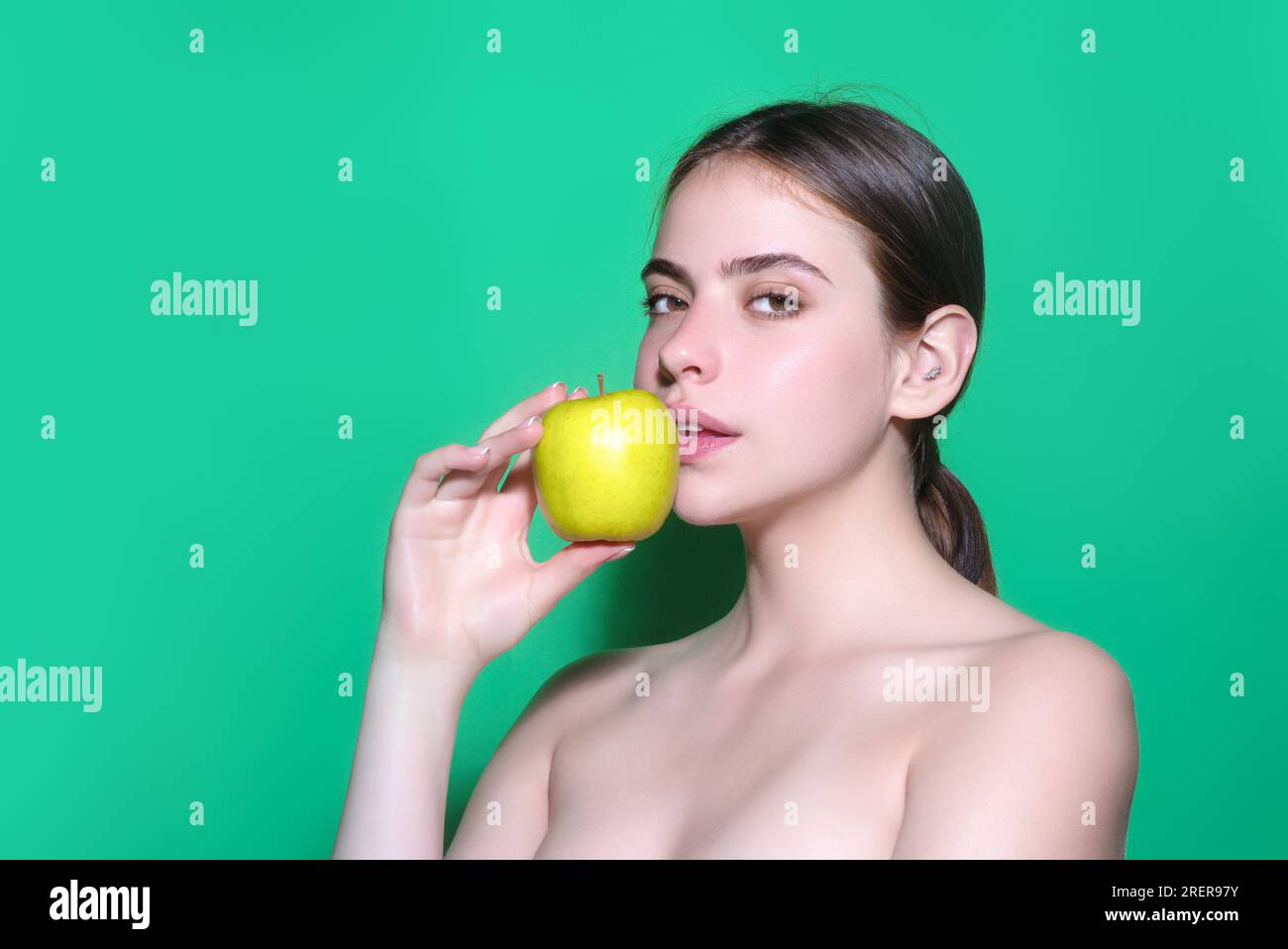 Junge Frau, die Apfel schlägt, gesunder Lebensstil. Mädchen haben ein frisches, grünes Apfelporträt auf grünem, isoliertem Hintergrund. Gesundes Essen. Obst für Stockfoto