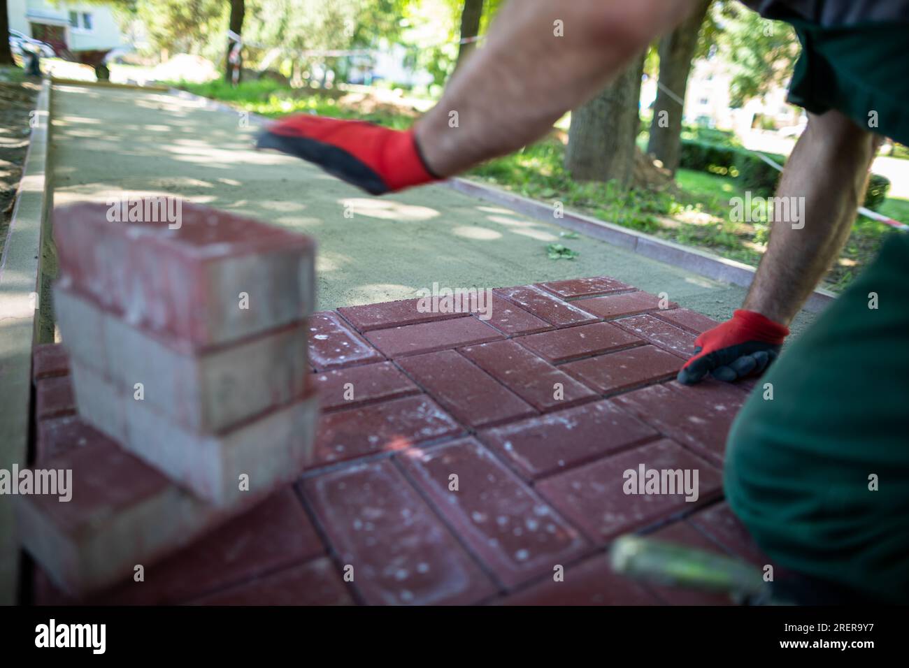 Ein Bauarbeiter kniet nieder, um Pflastersteine an einem sonnigen Tag zu legen. Stockfoto