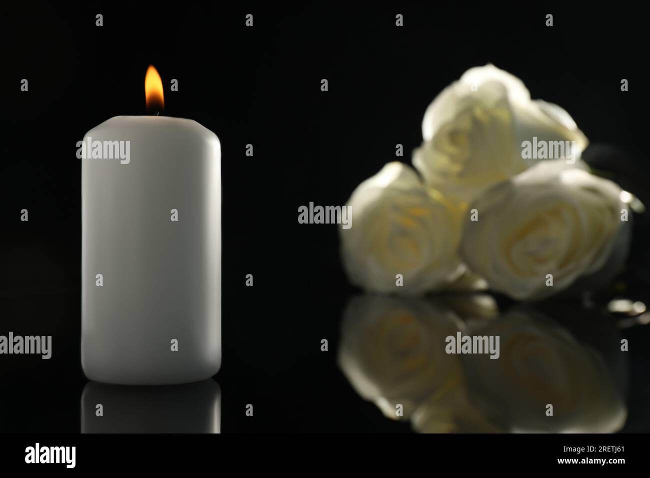 Weiße Rosen und brennende Kerze auf schwarzer Spiegeloberfläche in der Dunkelheit, Nahaufnahme mit Platz für Text. Begräbnissymbole Stockfoto