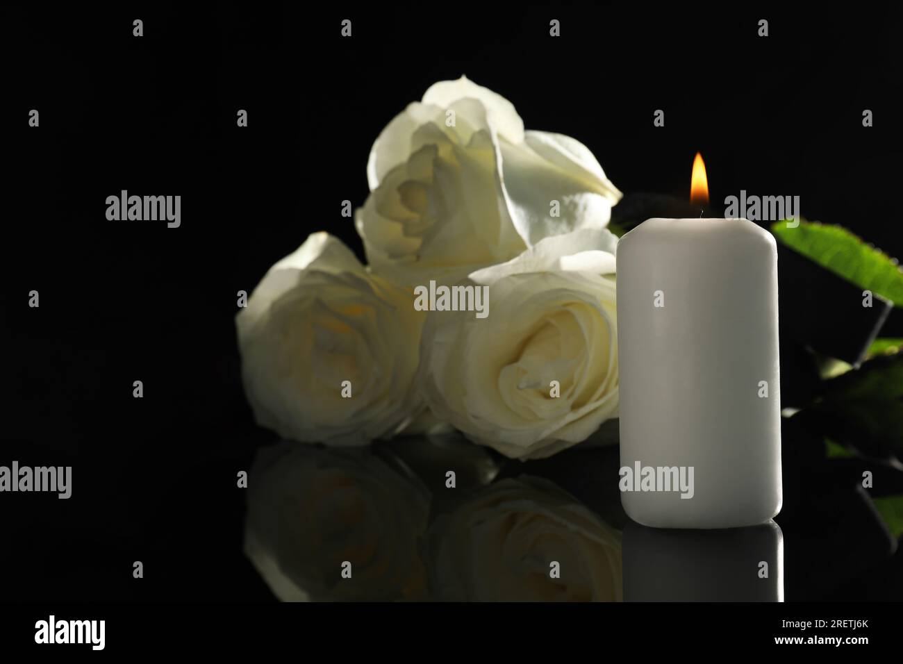 Weiße Rosen und brennende Kerze auf schwarzer Spiegeloberfläche bei Dunkelheit, Platz für Text. Begräbnissymbole Stockfoto