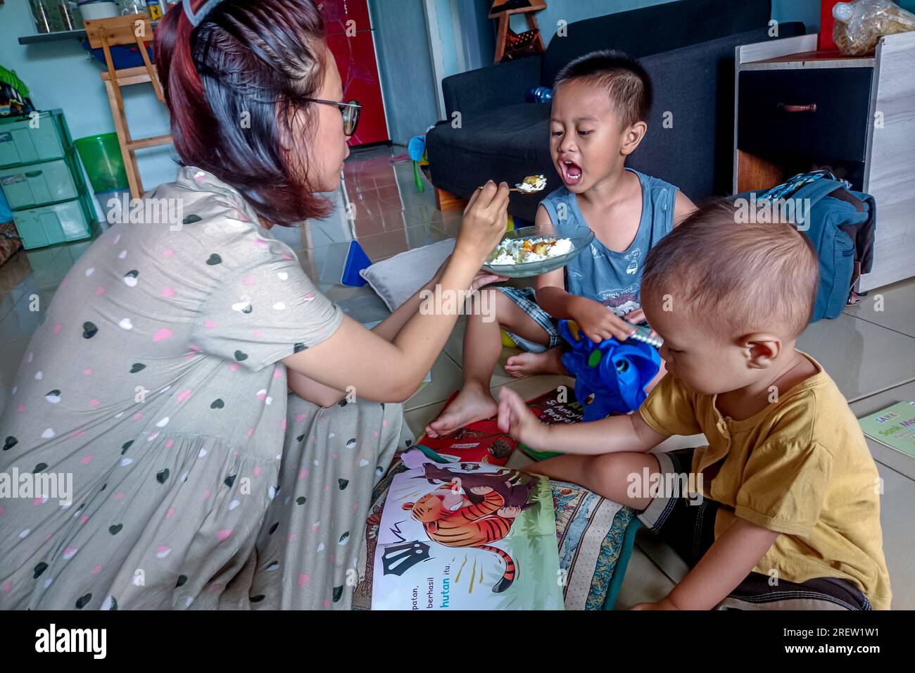 Mutter und kleiner Sohn frühstücken, während sie sich zusammen Bilderbücher anschauen Stockfoto