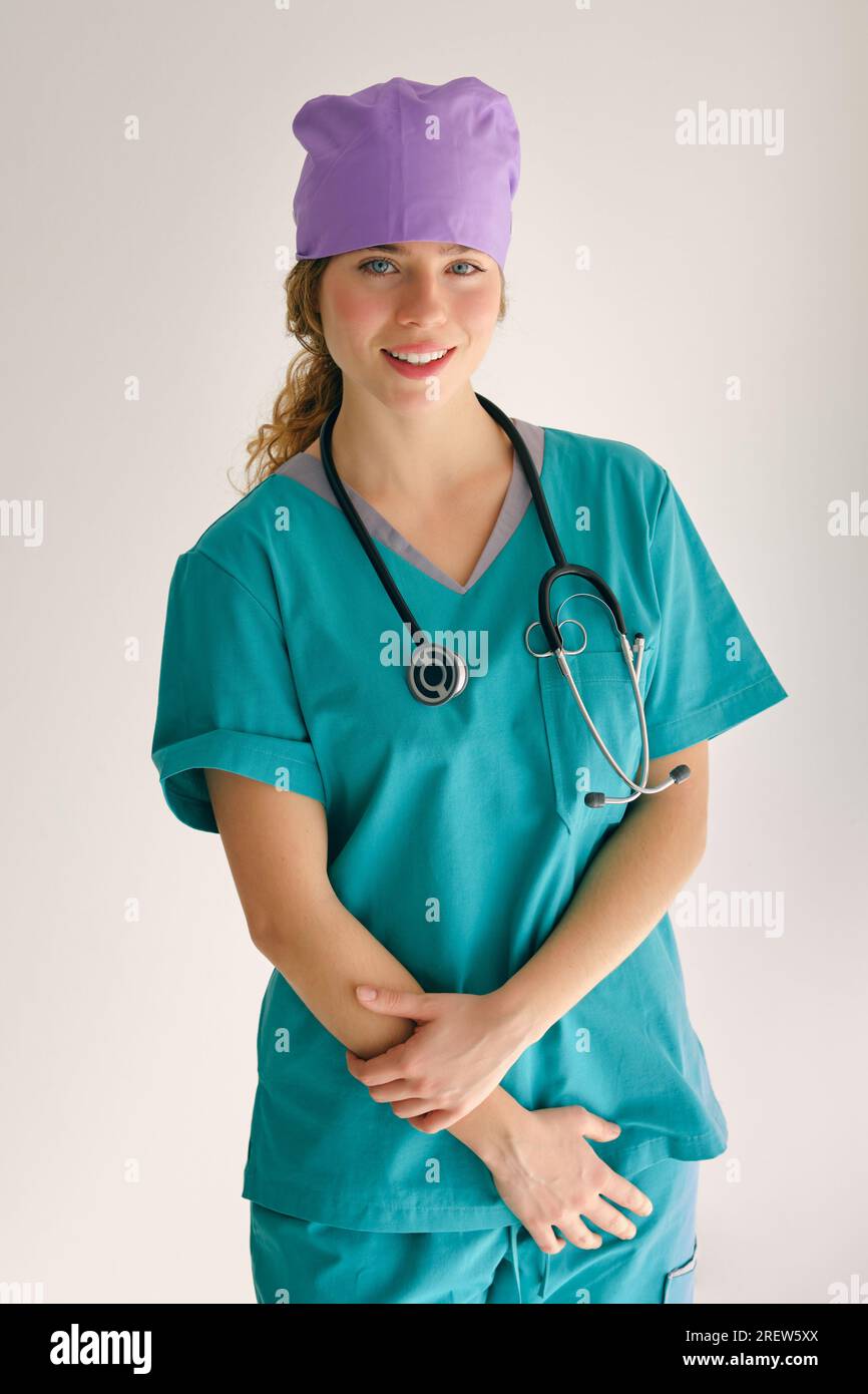 Positive Frau in grüner medizinischer Arbeitskleidung und Stethoskop, die auf die Kamera schaut, während sie im Studio steht Stockfoto
