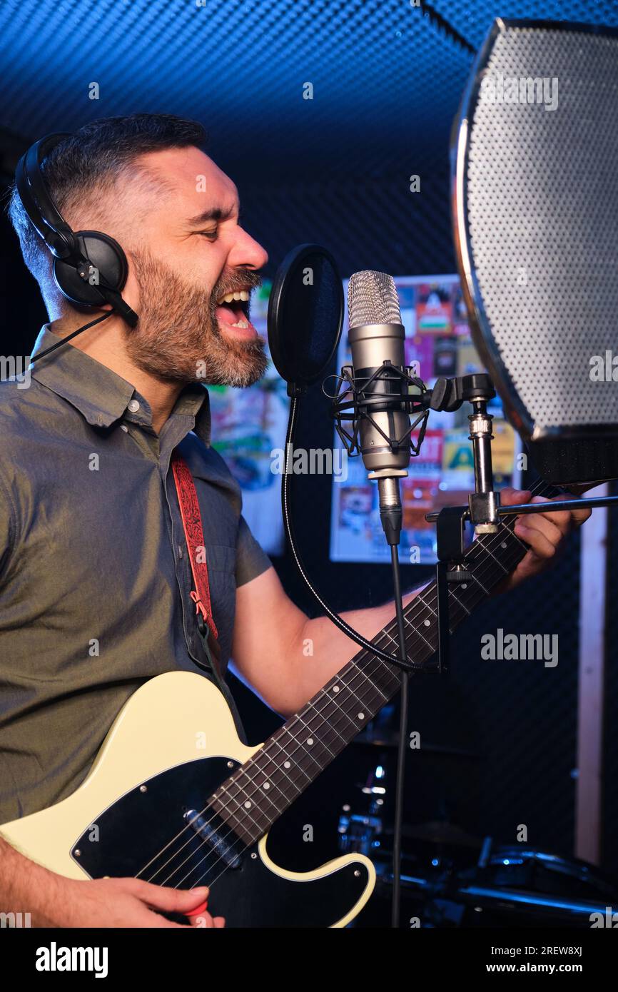 Sänger und Gitarrist mit Kopfhörern, die ein neues Album in einem Aufnahmestudio aufnehmen. Stockfoto