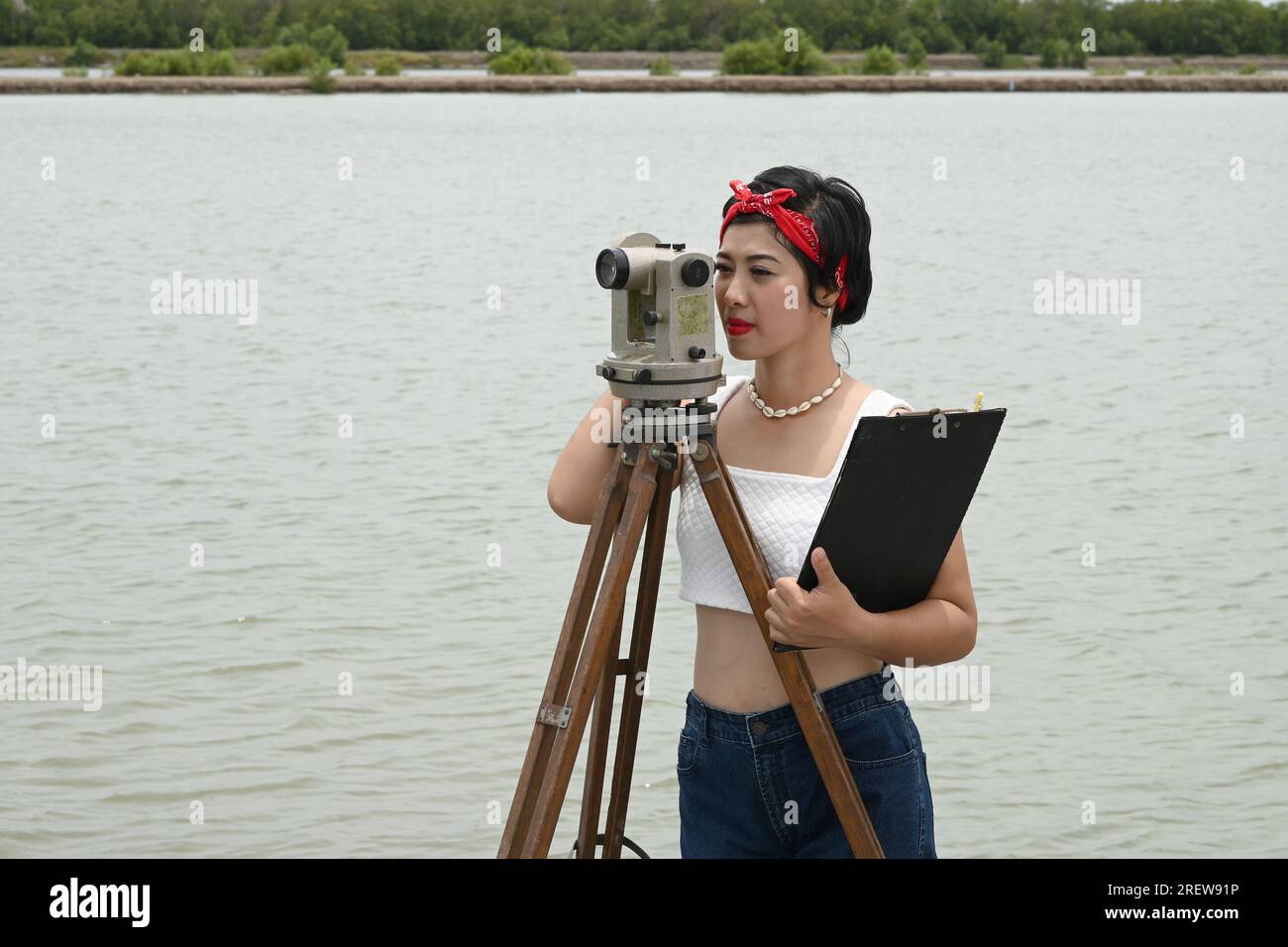 Hübsche asiatische Vermessungsfrau oder Ingenieurin, die mit Theodolith-Transitgeräten auf einer Baustelle im Freien arbeitet. Stockfoto