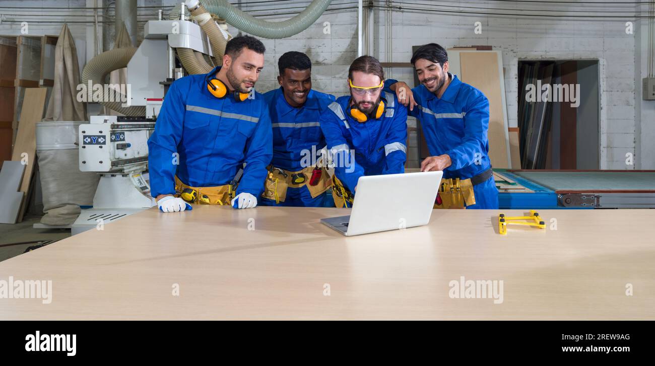 Eine Gruppe von Bauarbeitern hat sich in einem Industriebetrieb in Laptopdaten vertieft, umgeben von Maschinen, inmitten eines Klappens der Produktivität, und zeigte Stockfoto