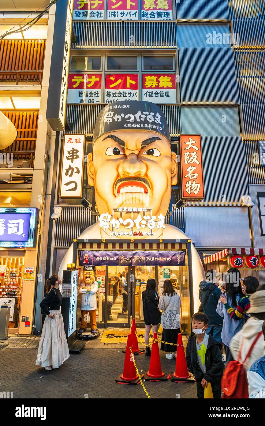 Die berühmte Fassade des Restaurants Kushikatsu daruma in Dotonbori, Osaka, bei Nacht. Eintritt mit der Gesichtsskulptur „wütender Koch“, die oben beleuchtet ist. Stockfoto