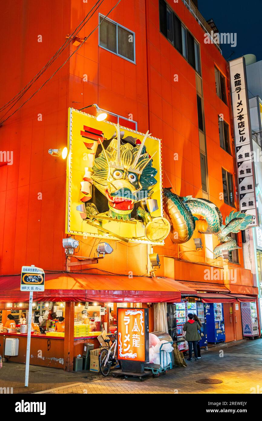 Kinryu Ramen Restaurant, orangefarbenes Gebäude in Dotonbori, Osaka. Nachtaufnahme, mit der berühmten Drachen-Skulptur, beleuchtet, über dem Take-Away-Schalter, Stockfoto