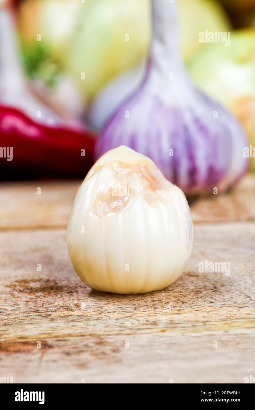 Verdorbene Knoblauchzehen auf dem Küchentisch, während ein Gericht mit Knoblauch gekocht und auf einem Schneidebrett geschnitten wird Stockfoto