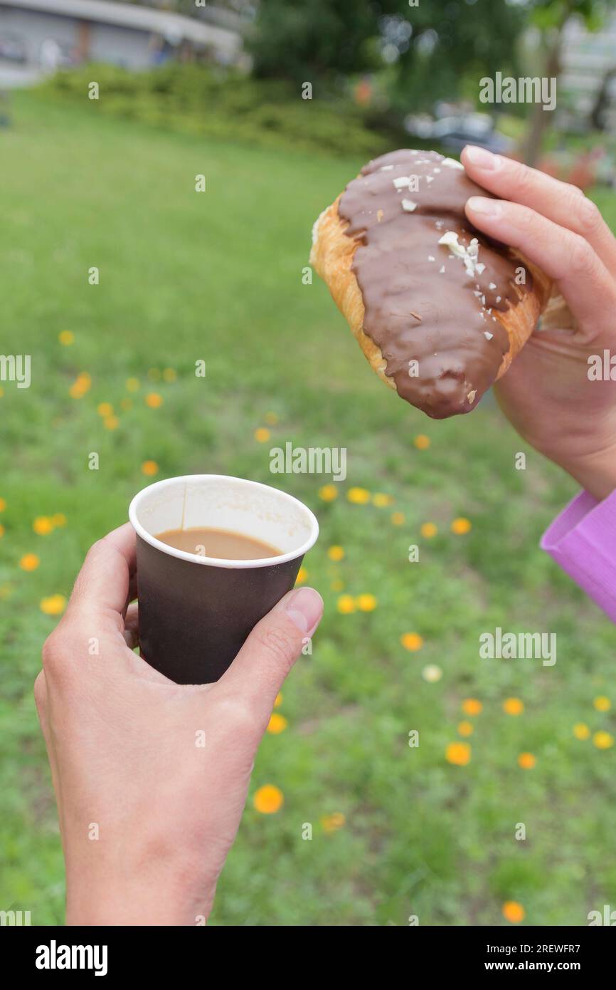 Schokoladen-Croissant und Kaffee in einem Pappbecher in den Händen einer Frau. Schnelles Frühstück Stockfoto