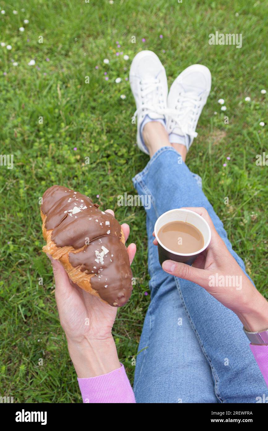 Kaffee in einem Pappbecher und Schokoladen-Croissant in den Händen einer Frau. Vertikal Stockfoto