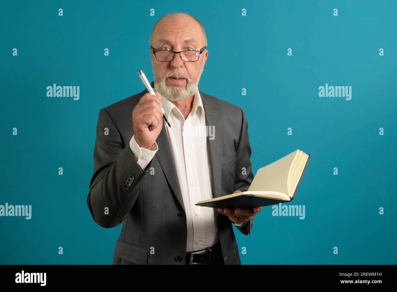 Ein älterer Mann in einem Anzug mit Notizbuch und Stift denkt über eine Aufgabe nach - auf blauem Hintergrund Stockfoto