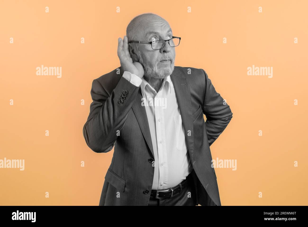 Älterer Mann in der Pose des Lauschens bei einem Gespräch. Ein Mann, der versucht zuzuhören. Die Hand wird an das Ohr gehalten. Heller orangefarbener Hintergrund. Kunst Stockfoto