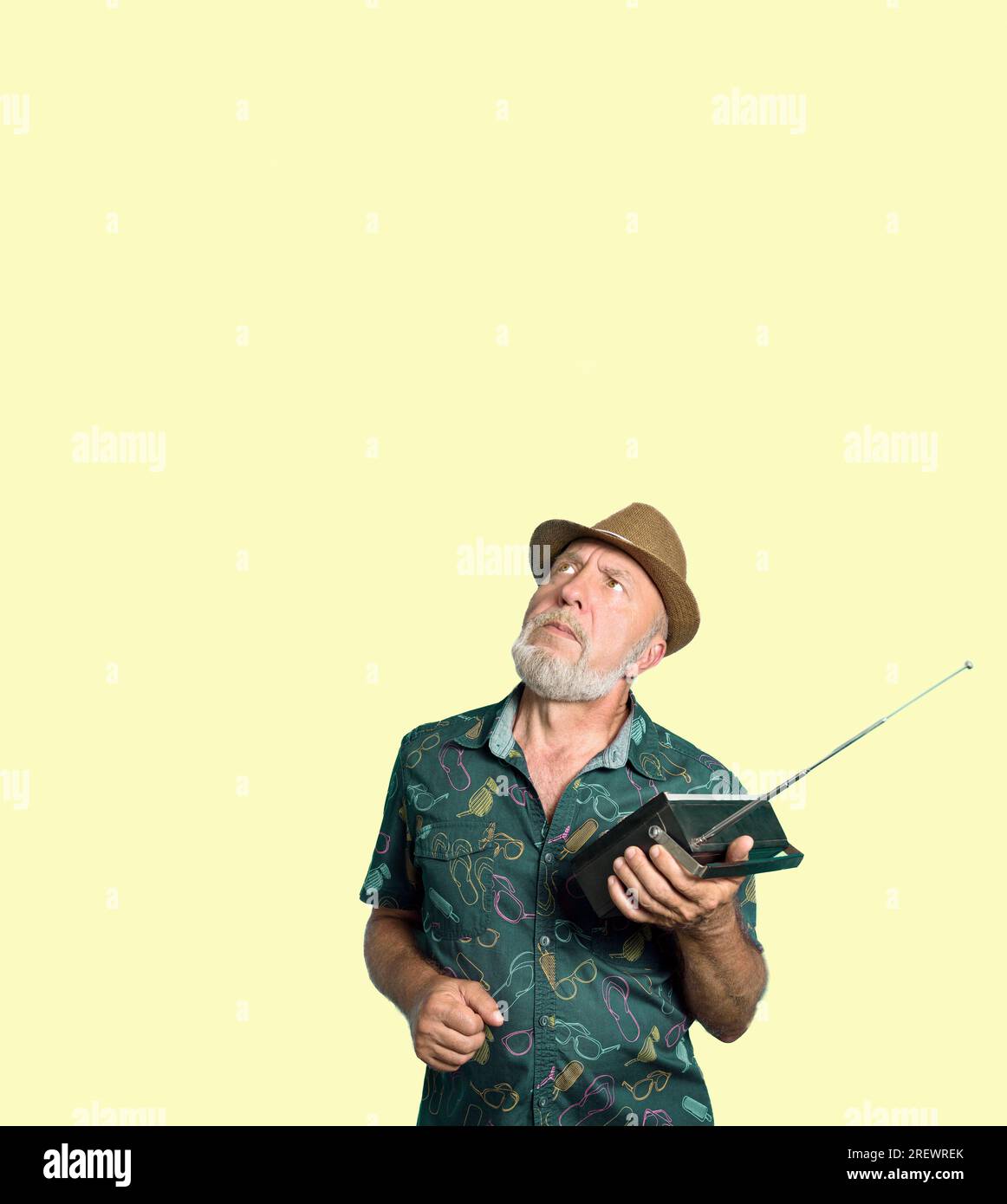 Ein Gentleman mit Hut hört ein altes Radio auf gelbem Hintergrund. Eindrücke von den Nachrichten im Radio. Stockfoto