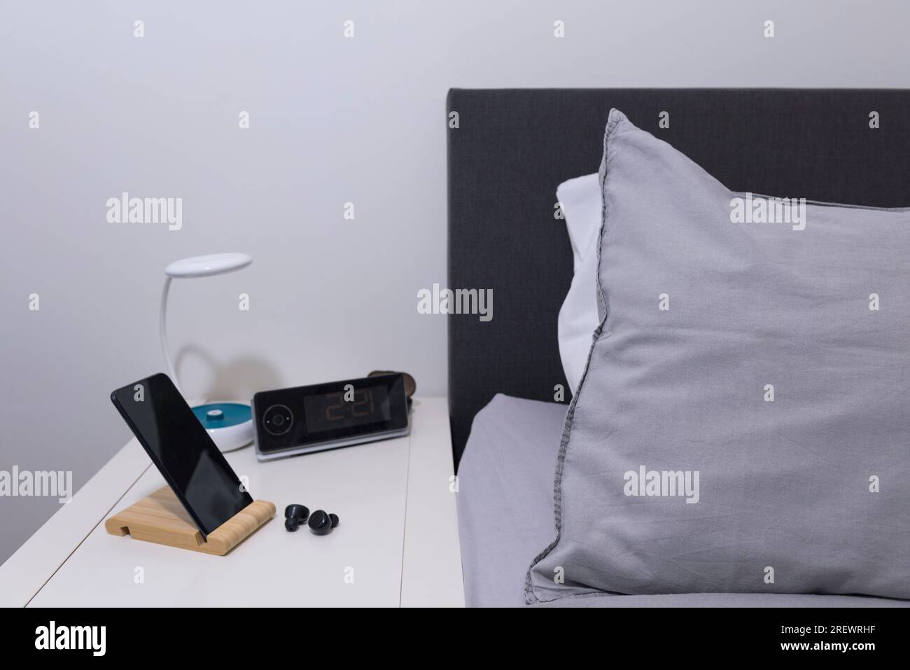 Richtiges Schlafzimmer. Smartphone und Headset auf dem Nachttisch mit Lampe und Uhr Stockfoto
