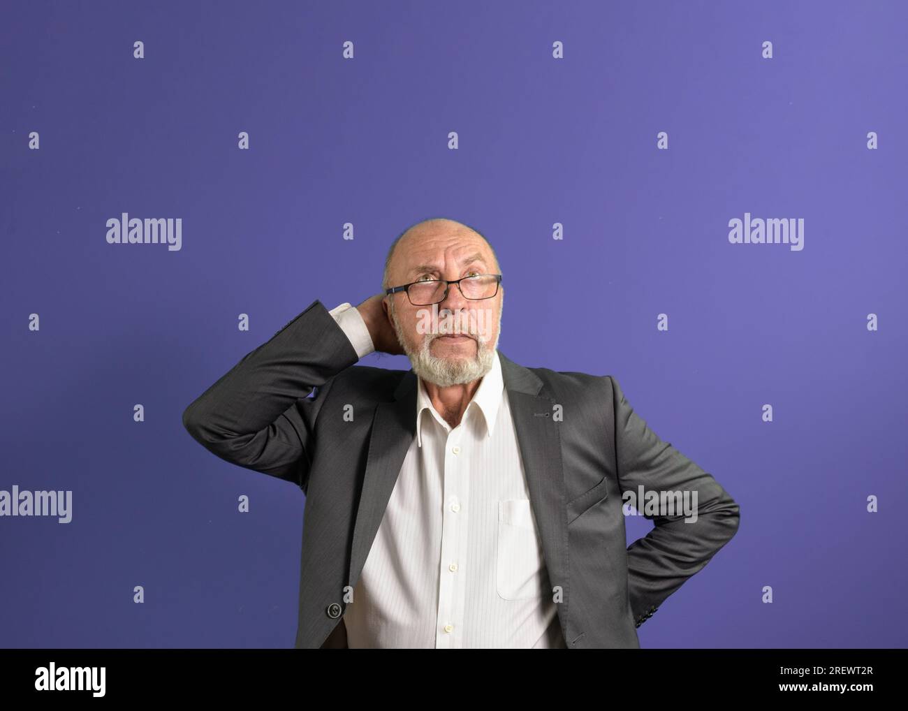 Porträt eines älteren Mannes mit Bart und Brille, blickt mit Bedacht auf. Platz für Text. Violetter Hintergrund Stockfoto