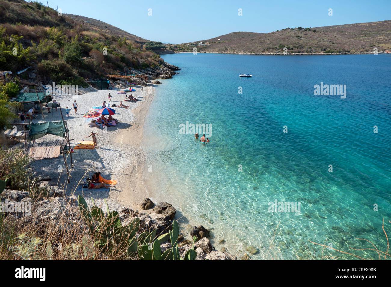 Blick auf den abgeschiedenen und idyllischen Strand in der Nähe von Porto Palermo, Albanien, mit Menschen, die schwimmen und Spaß haben. Touristen genießen den Sommer in Albanien Stockfoto