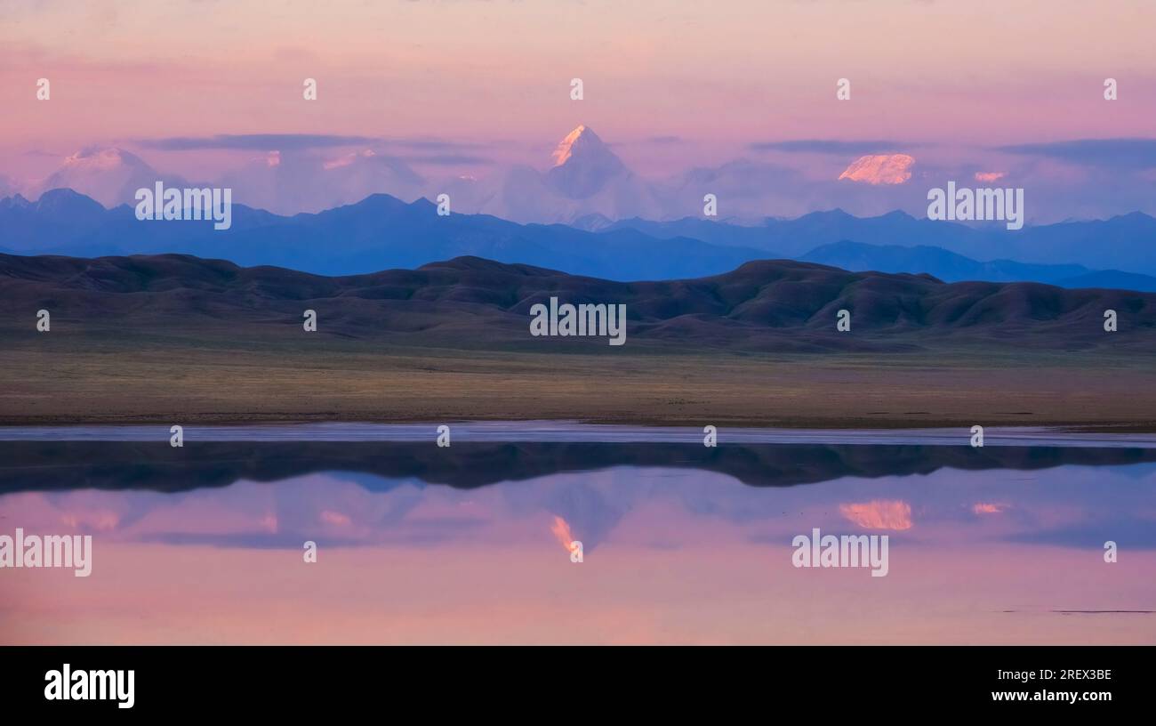 Der große Berg Khan Tengri erhebt sich während eines rosa Morgens über andere Berge und spiegelt sich im Wasser des Tuzkol-Salzsees in Kasachstan wider Stockfoto