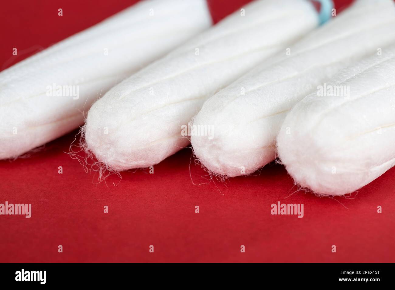 Damenhygienetampon auf rotem Hintergrund, Hygienetampon aus Baumwolle und anderen Materialien, Nahaufnahme auf roter Papieroberfläche Stockfoto