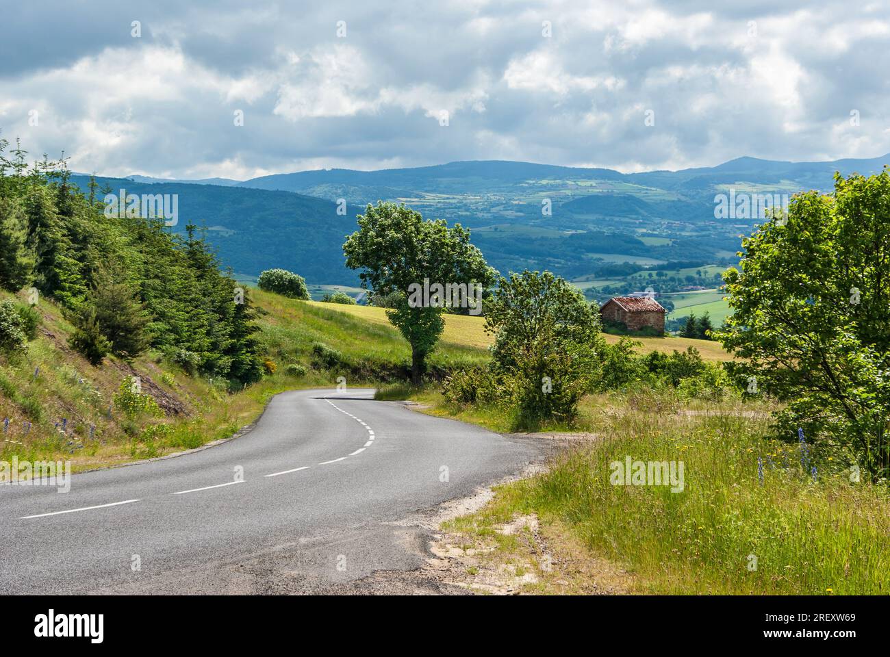 Ländliche Landschaft mit Landstraße in französischer landwirtschaftlicher Landschaft und Bergen im Hintergrund. Stockfoto