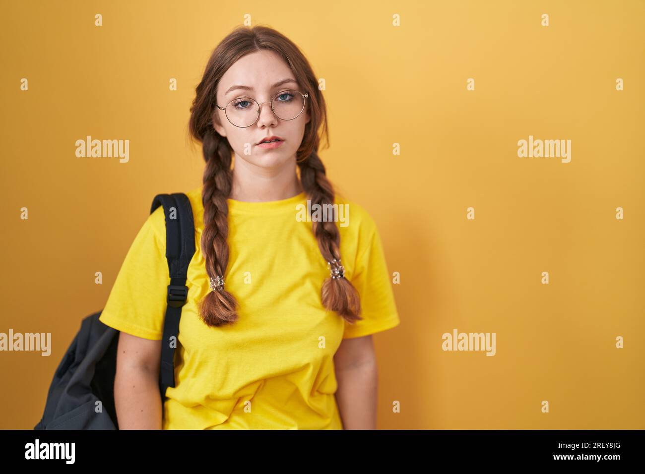 Junge weiße Frau, die einen Studentenrucksack auf gelbem Hintergrund trägt, schläfrig und müde aussieht, erschöpft wegen Müdigkeit und Kater, faule Augen im m Stockfoto