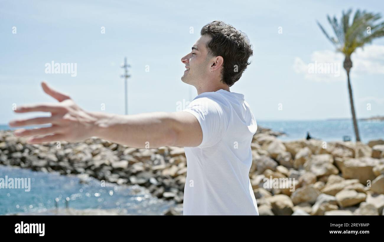 Junger lateinamerikanischer Mann atmet mit offenen Armen am Strand Stockfoto
