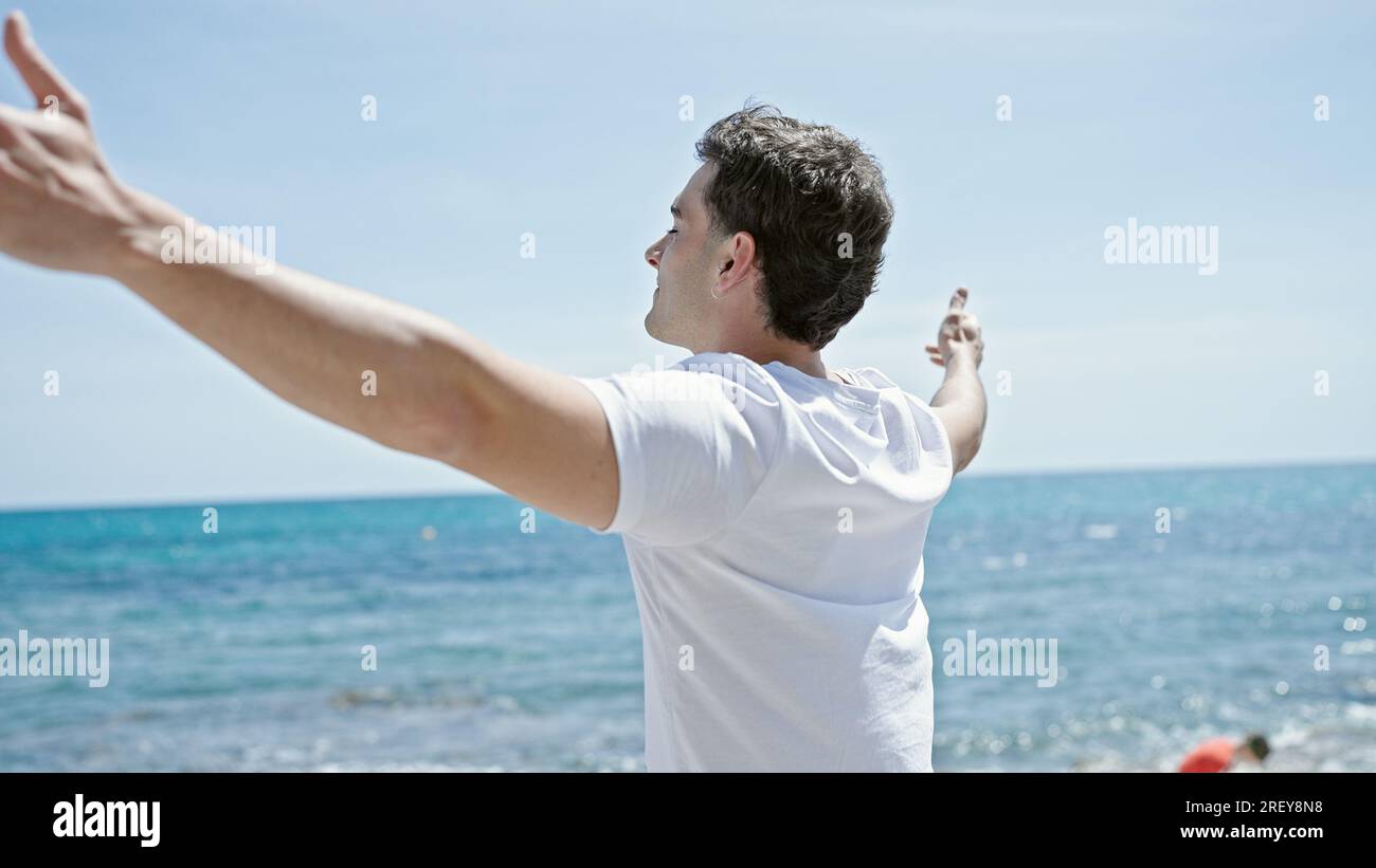 Junger lateinamerikanischer Mann atmet mit offenen Armen am Strand Stockfoto